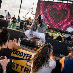 Stephen Thomas performing on stage at the Woody Fest with a heart visual on the screen behind him